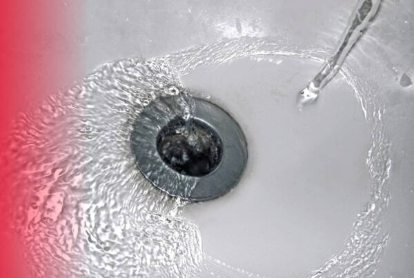 A top-down view of clear water swirling into a silver metal bathtub drain against a white tub surface.
