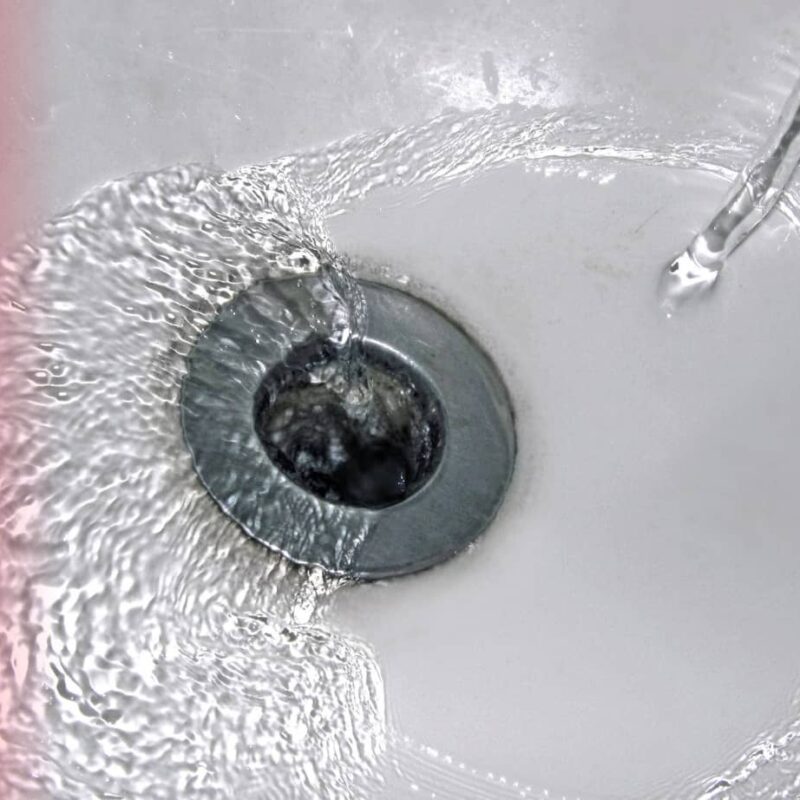 A top-down view of clear water swirling into a silver metal bathtub drain against a white tub surface.