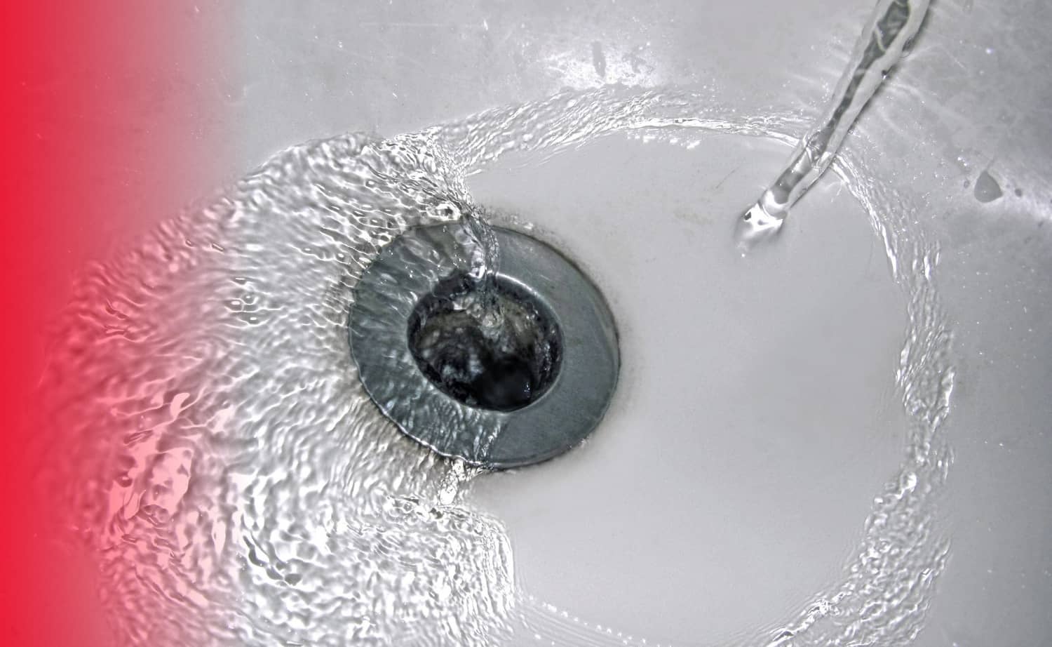 A top-down view of clear water swirling into a silver metal bathtub drain against a white tub surface.