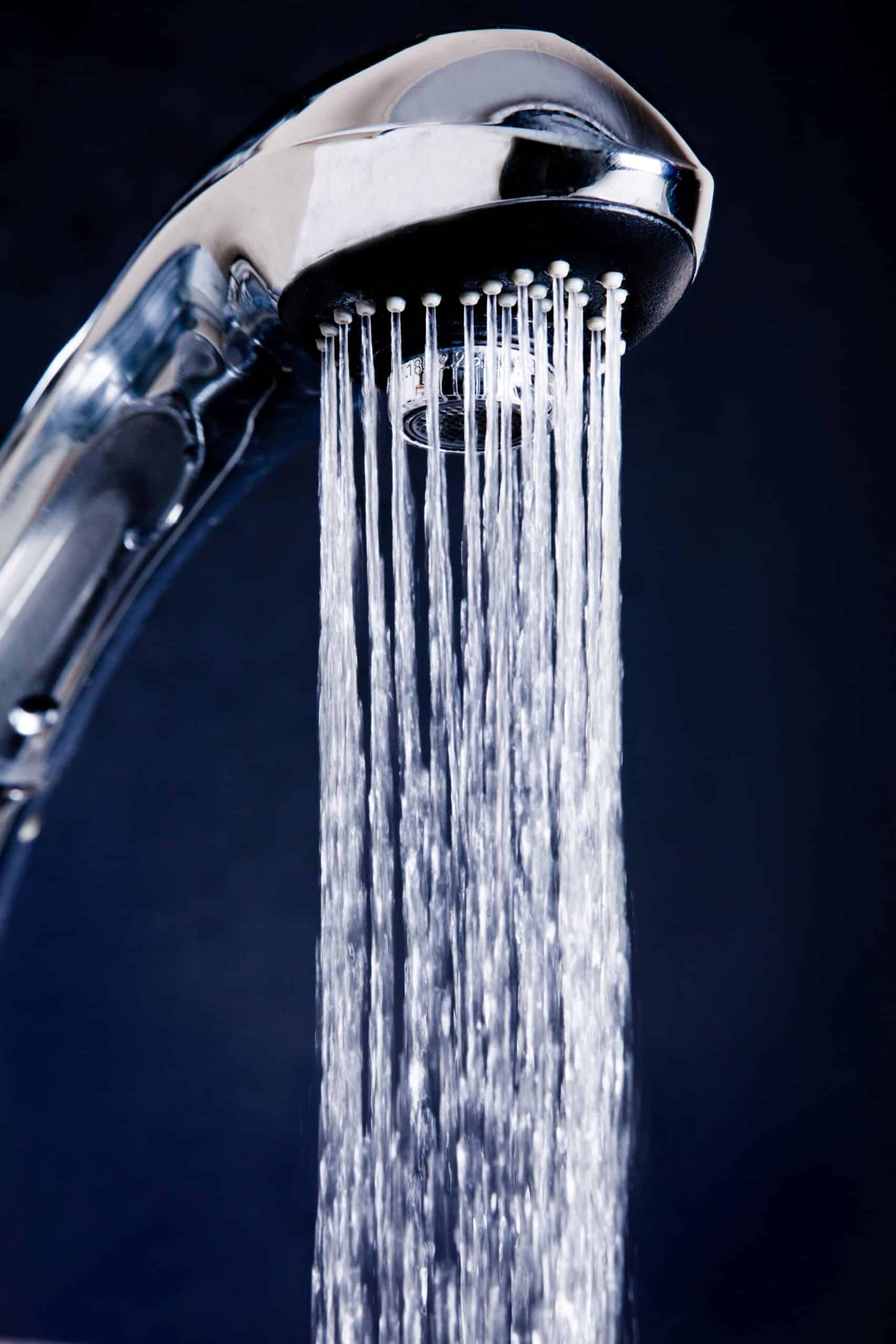 A close-up of a chrome kitchen faucet spray head with multiple streams of water flowing downward in a shower pattern against a dark background.