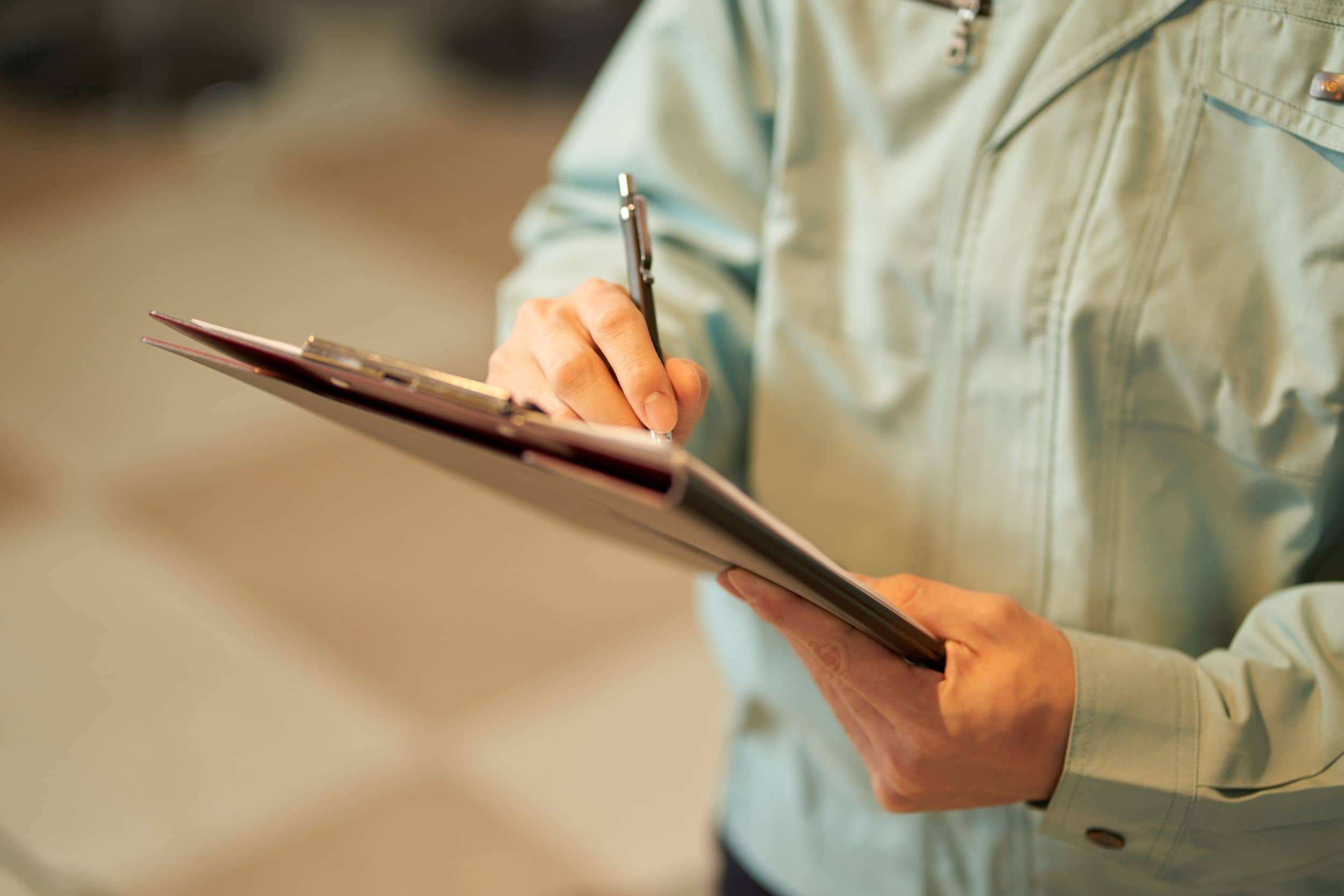 person in a light-colored work jacket writes on a clipboard with a pen.