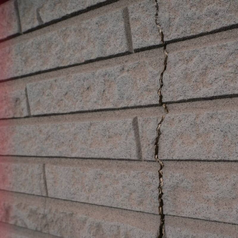 Close-up of textured grey cement siding shingles featuring a prominent vertical crack running through several panels.
